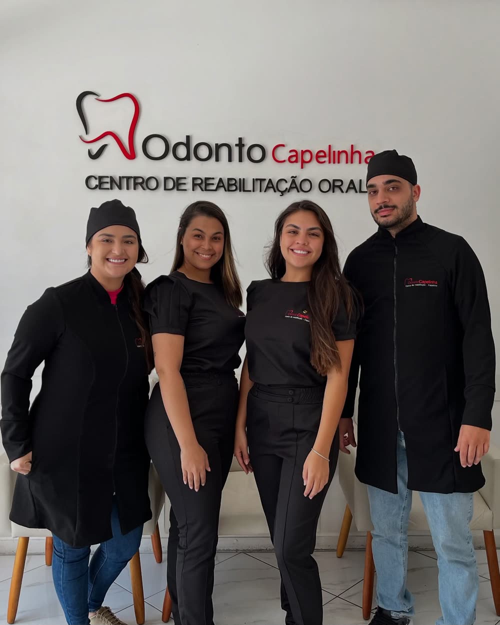 Equipe da Odonto Capelinha na recepção da clínica, sob a logo na parede